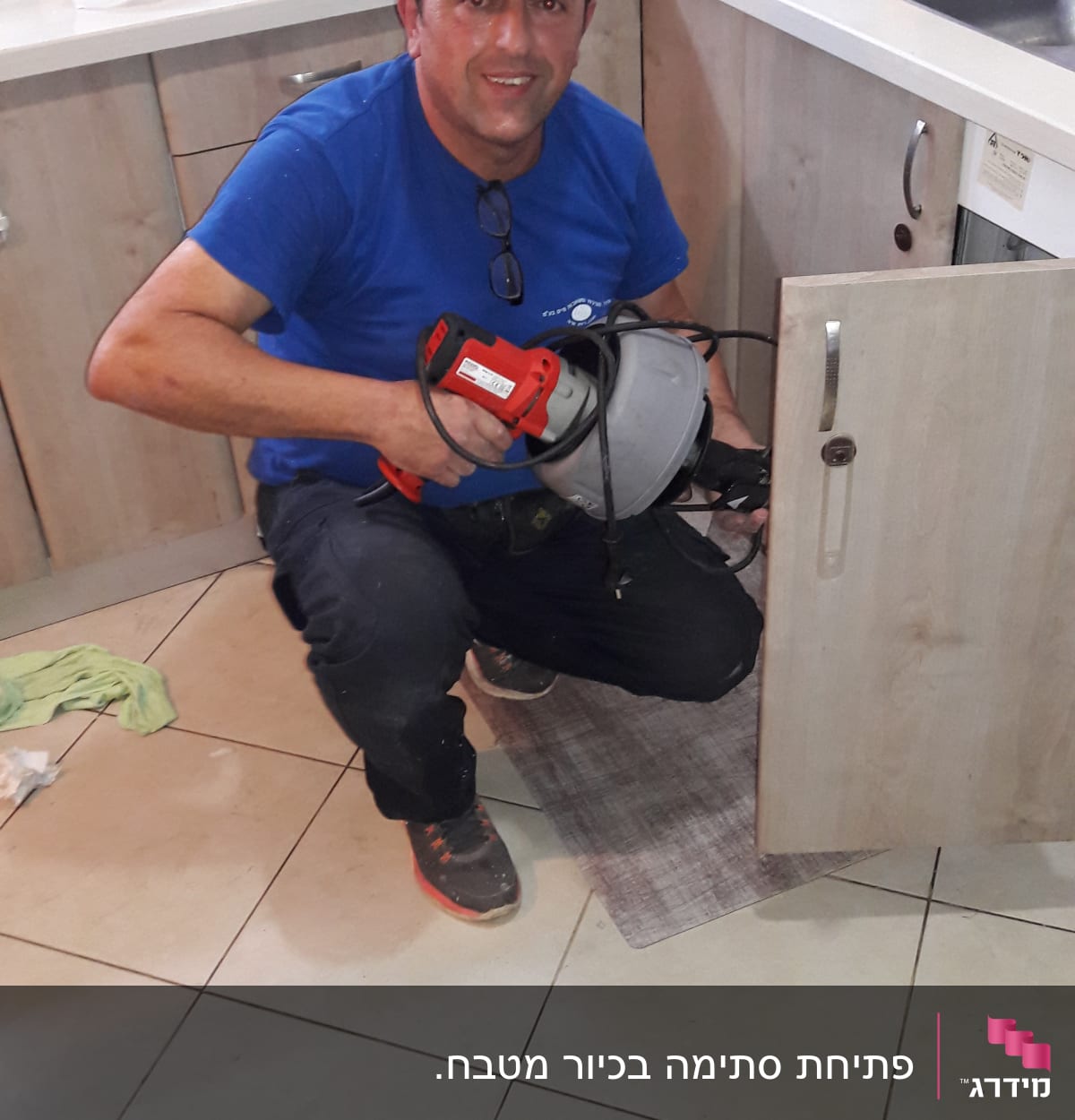 אדם מחזיק מכשיר אינסטלציה ליד ארון מטבח פתוח